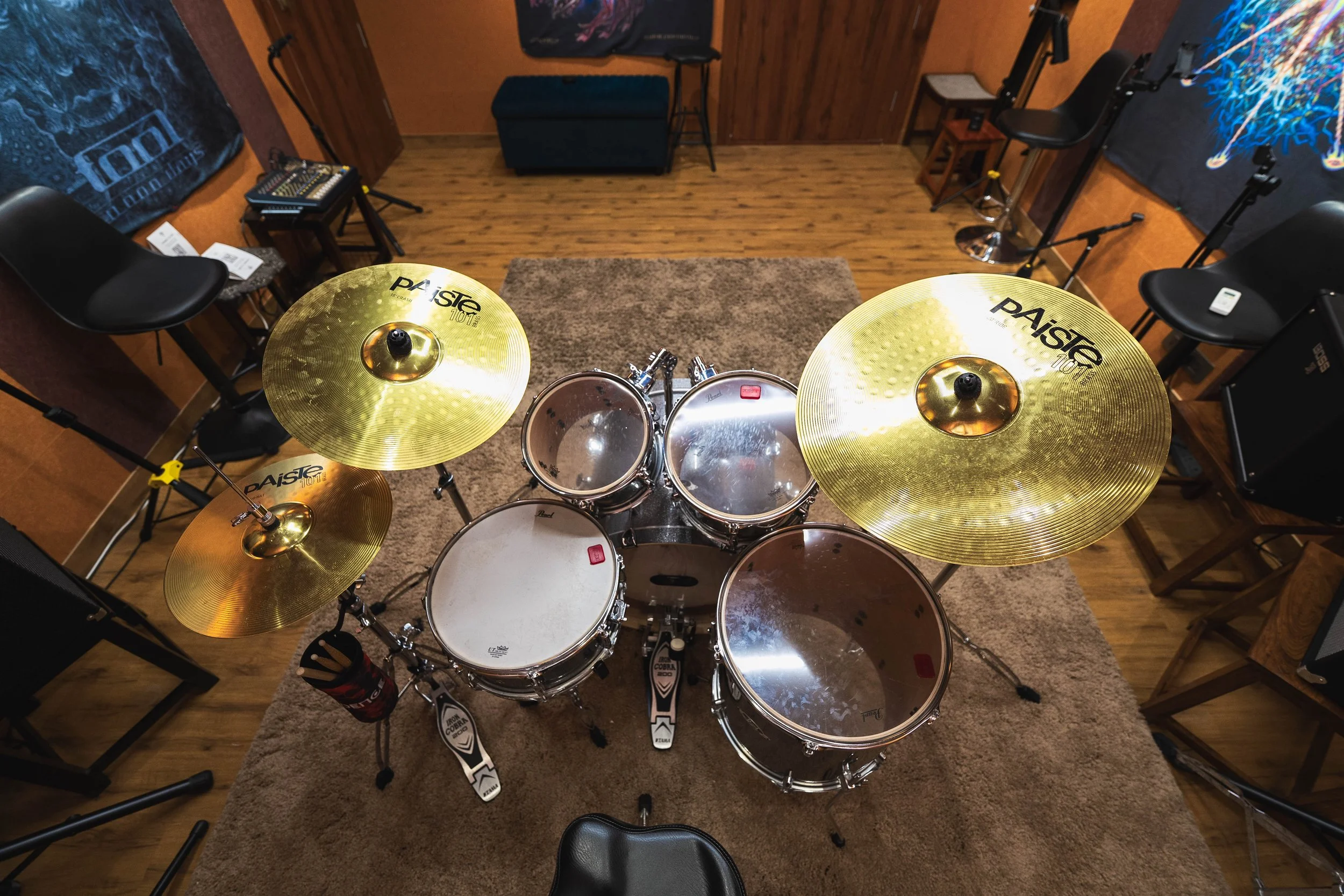 Top view of a drum set with cymbals in a music rehearsal room with chairs and musical posters on the walls.