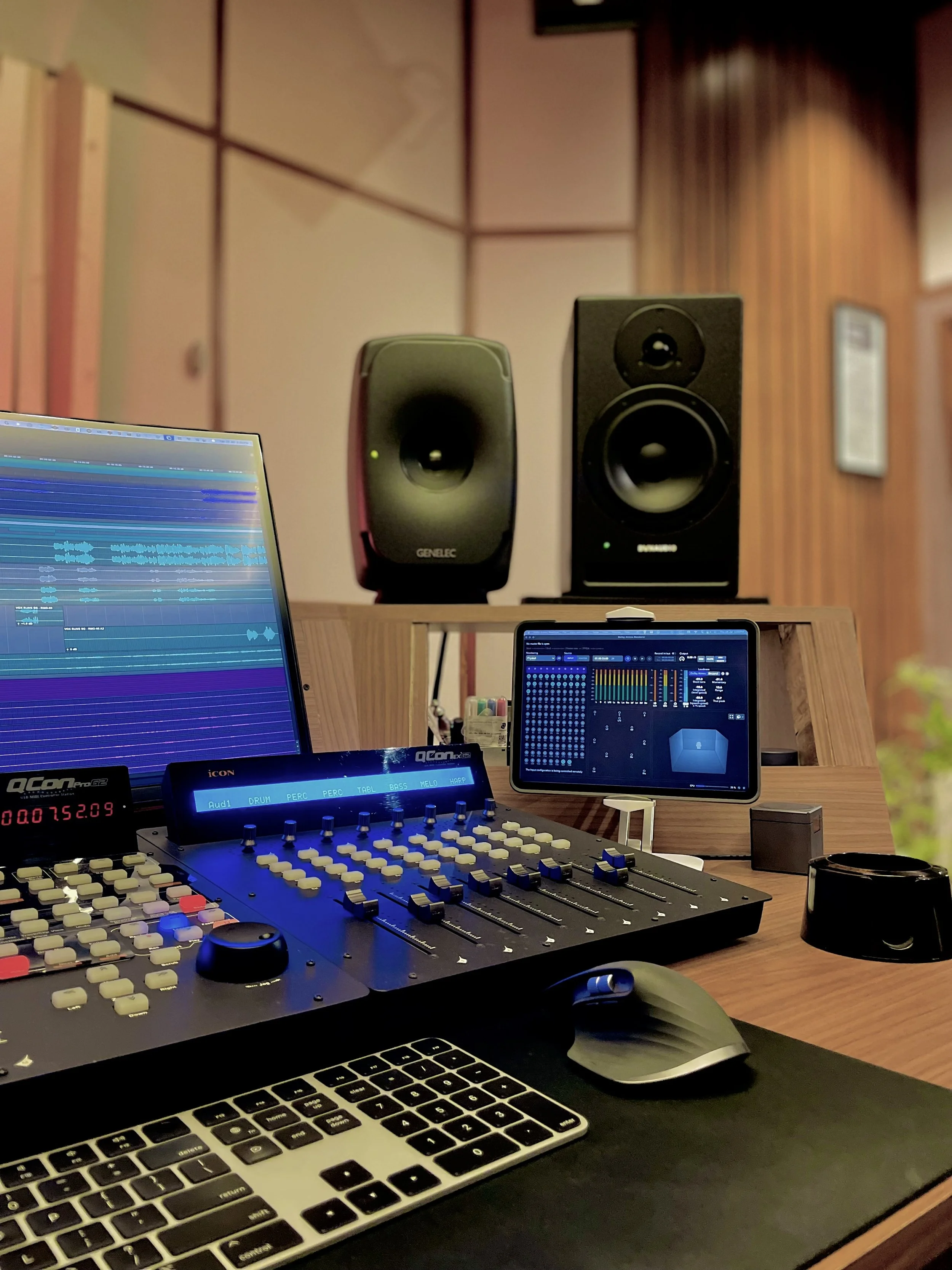 a control desk of a recording studio with a mixer, a screen, a keyboard, a mouse, an ipad and two speakers.