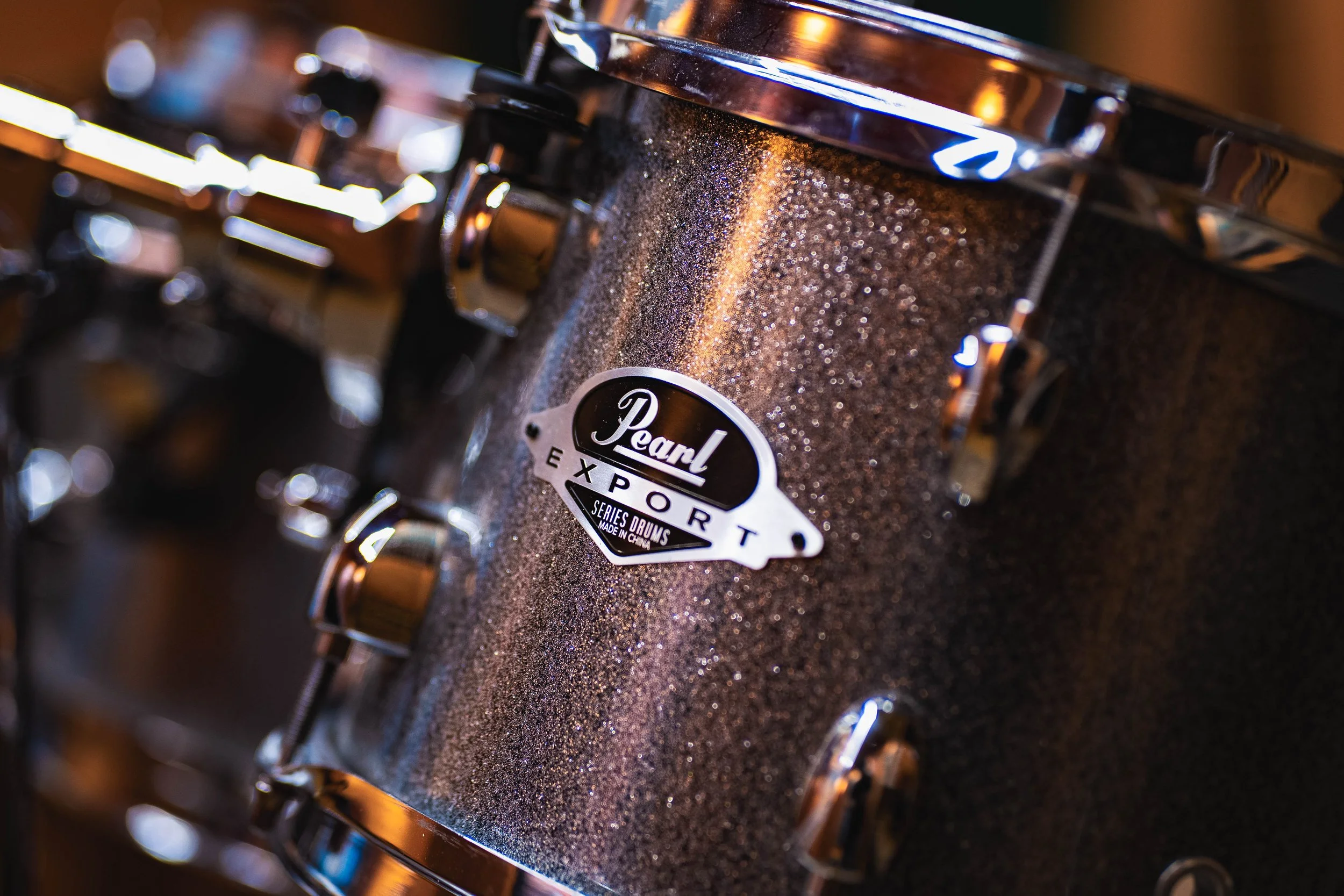 Close-up of a Pearl Export series drum with a dark, glittery finish, showing the tuning lugs and the Pearl logo.