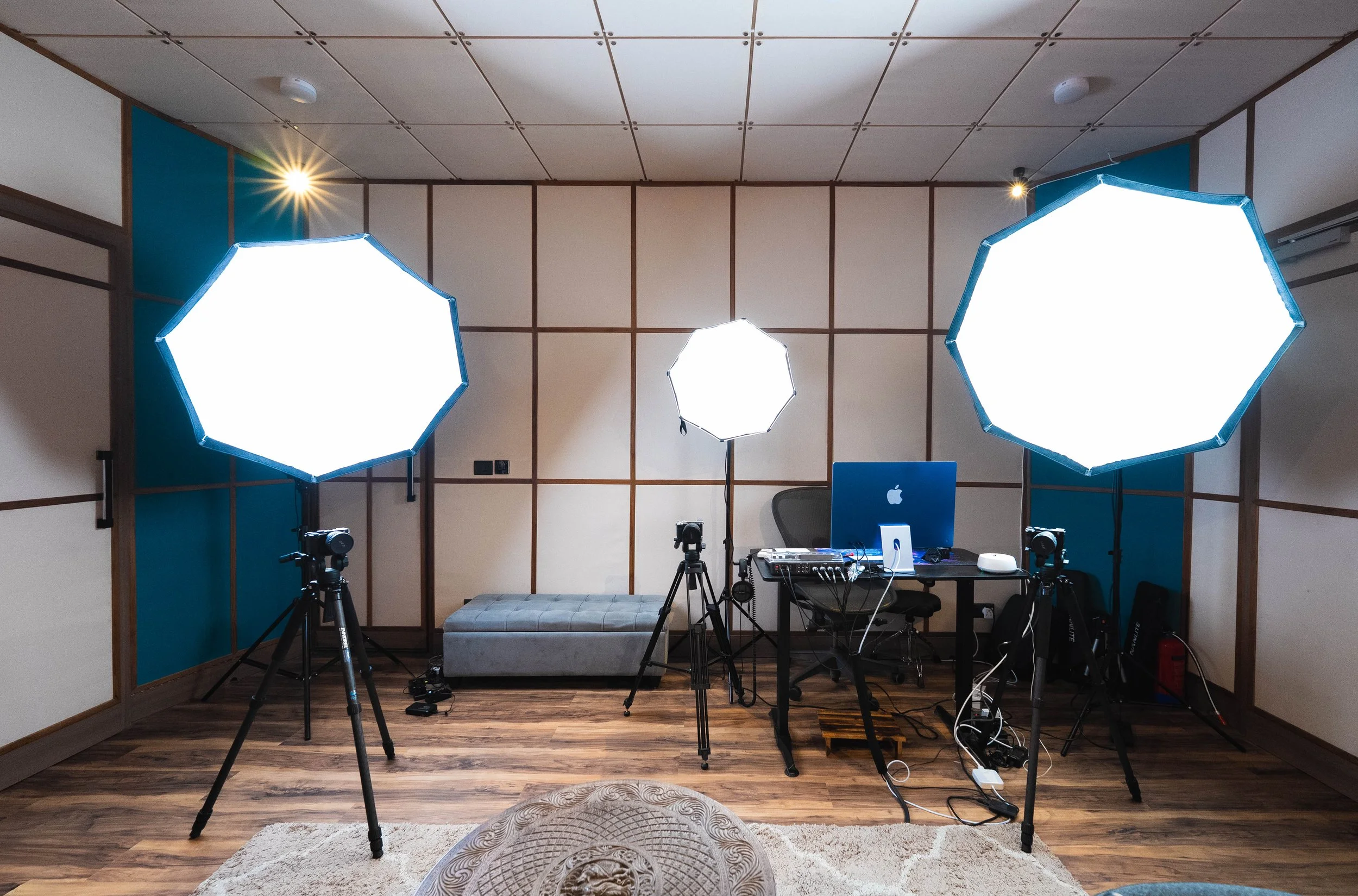 Three bright lights with cameras, a desk and a bench in a room