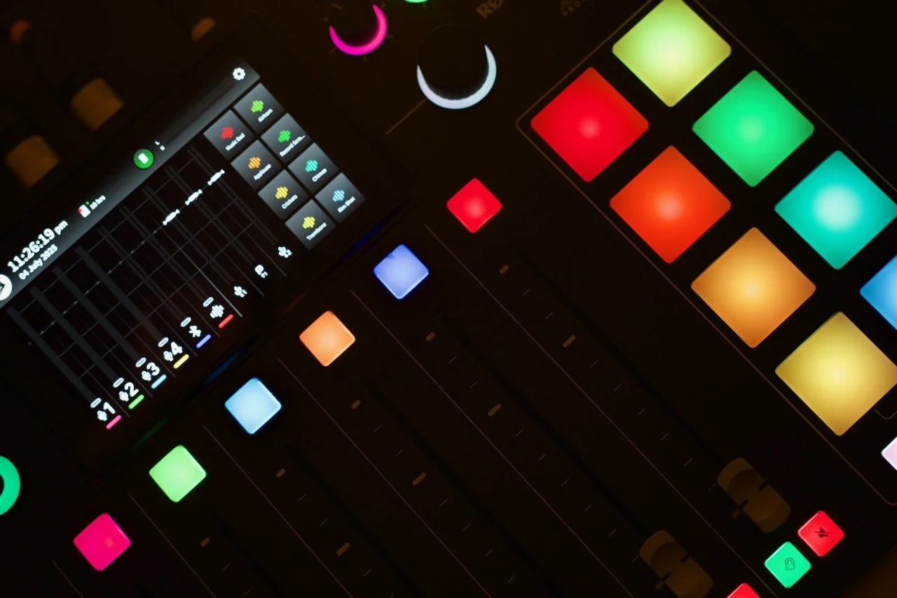 Close-up of a music production controller with colorful illuminated pad buttons and faders in a dimly lit setting.