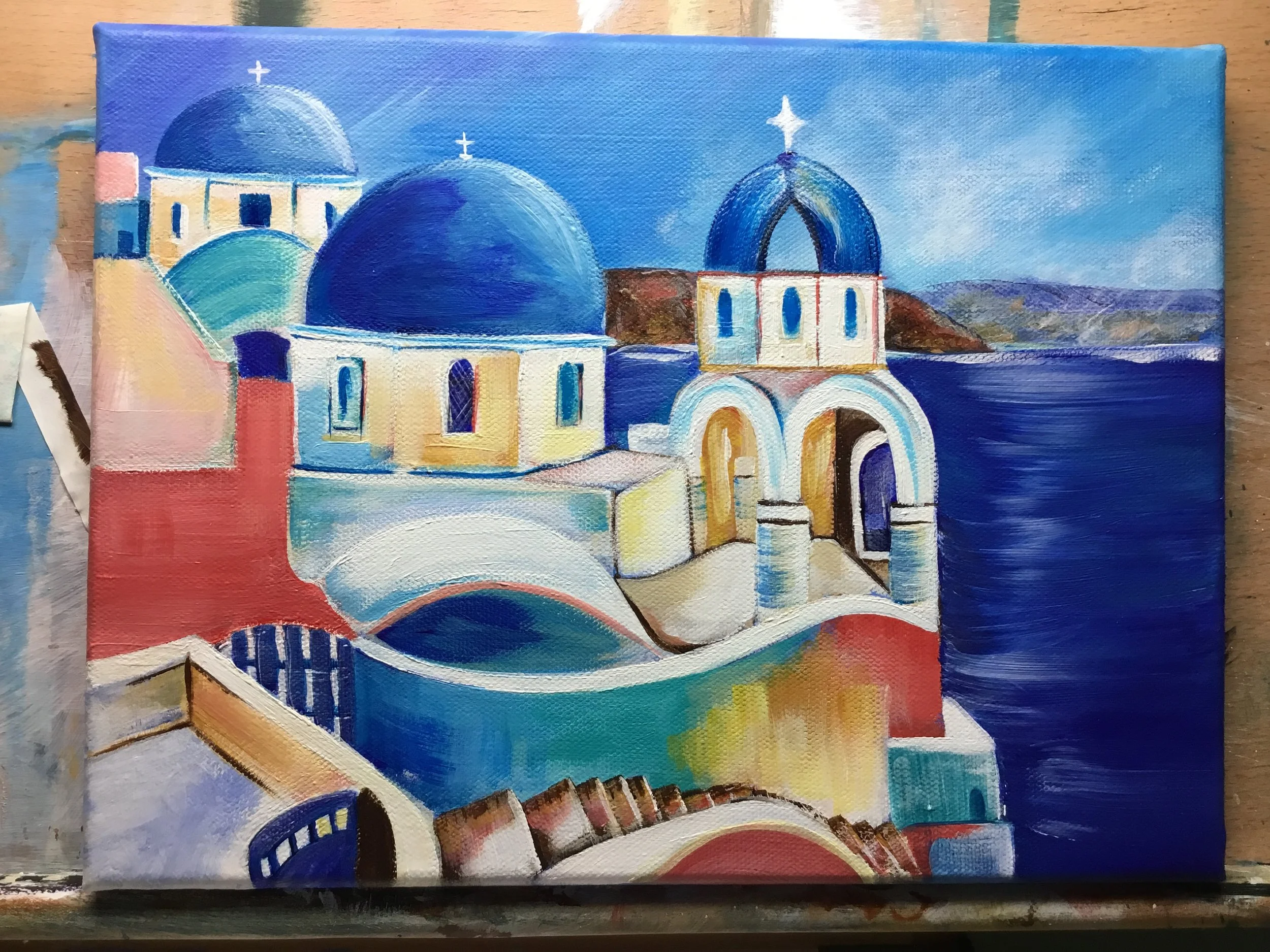Painted landscape of white buildings with blue domes and arches, characteristic of Greek architecture, with a blue sky and distant hills.
