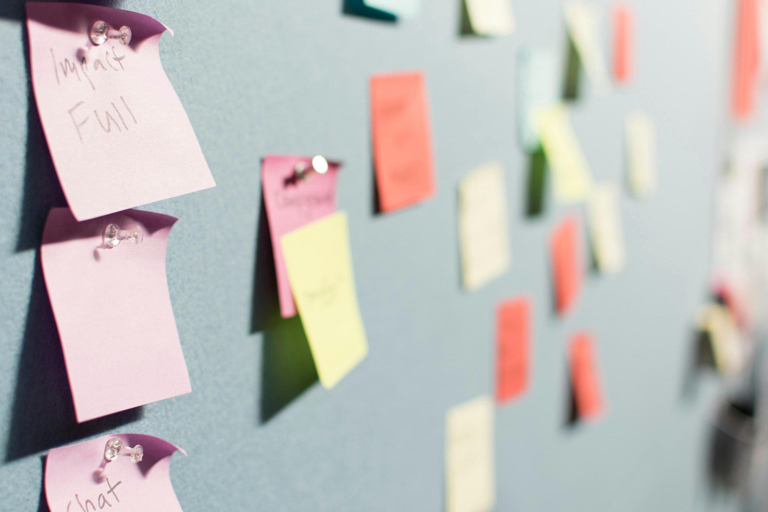 Colorful sticky notes pinned on a blue board, some are readable with words like 'Impact' and 'Full'. The notes are scattered, creating a brainstorming or planning scene.
