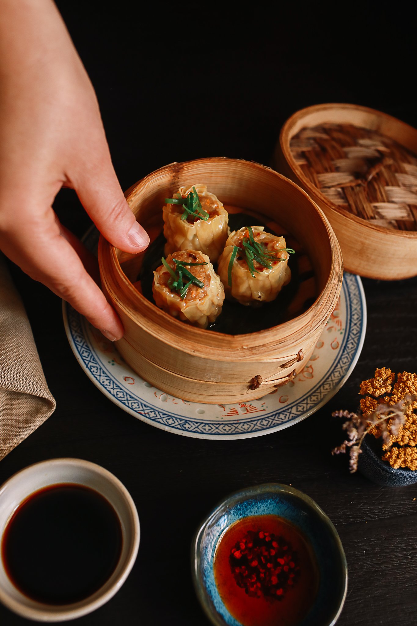 Hand holding bamboo steamer with siu mai dumplings
