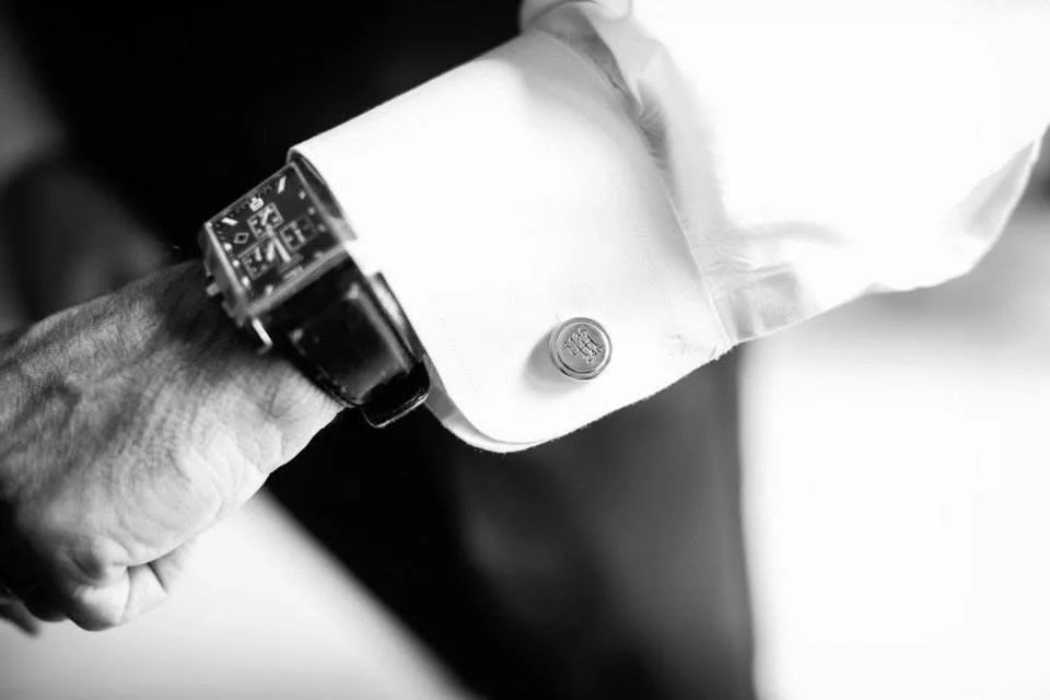 Black and white image of a person wearing a watch with a leather strap, and a dress shirt with a cufflink.