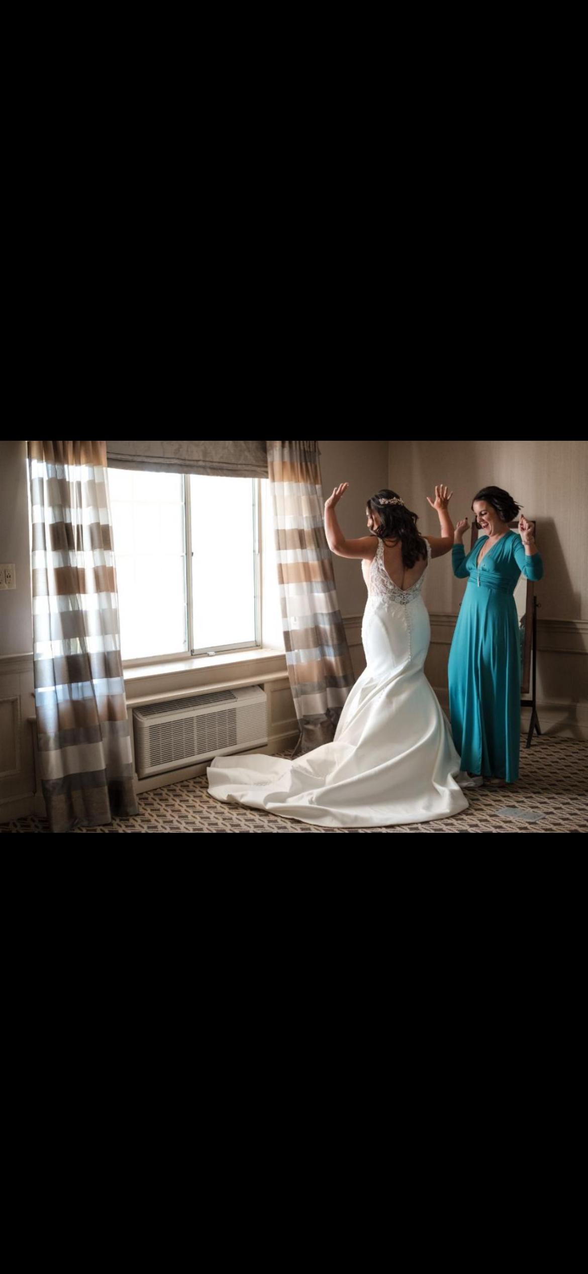 Bride in wedding dress and woman in teal dress facing large window