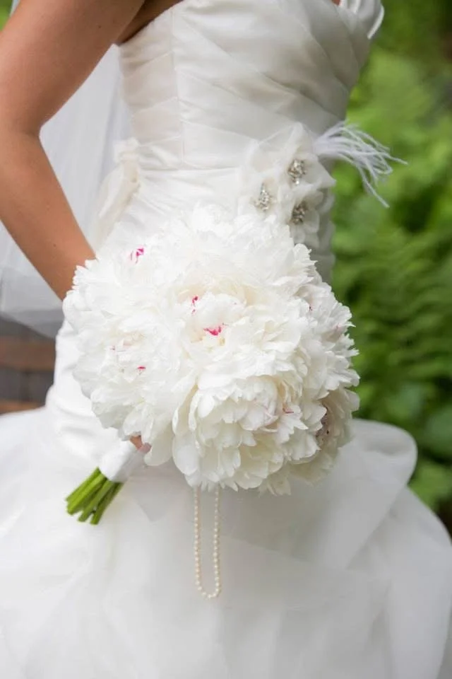 Bride in a white wedding dress holding a bouquet of white flowers with pearls, outdoors.