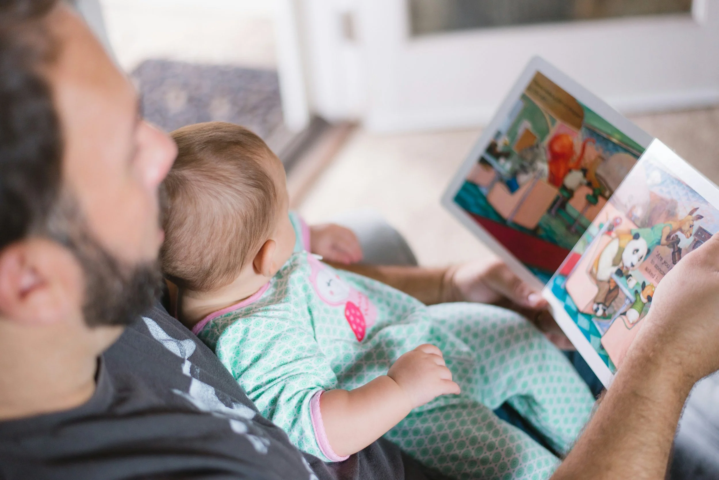 A man is holding a baby while reading a colorful Arabic-English children's book.