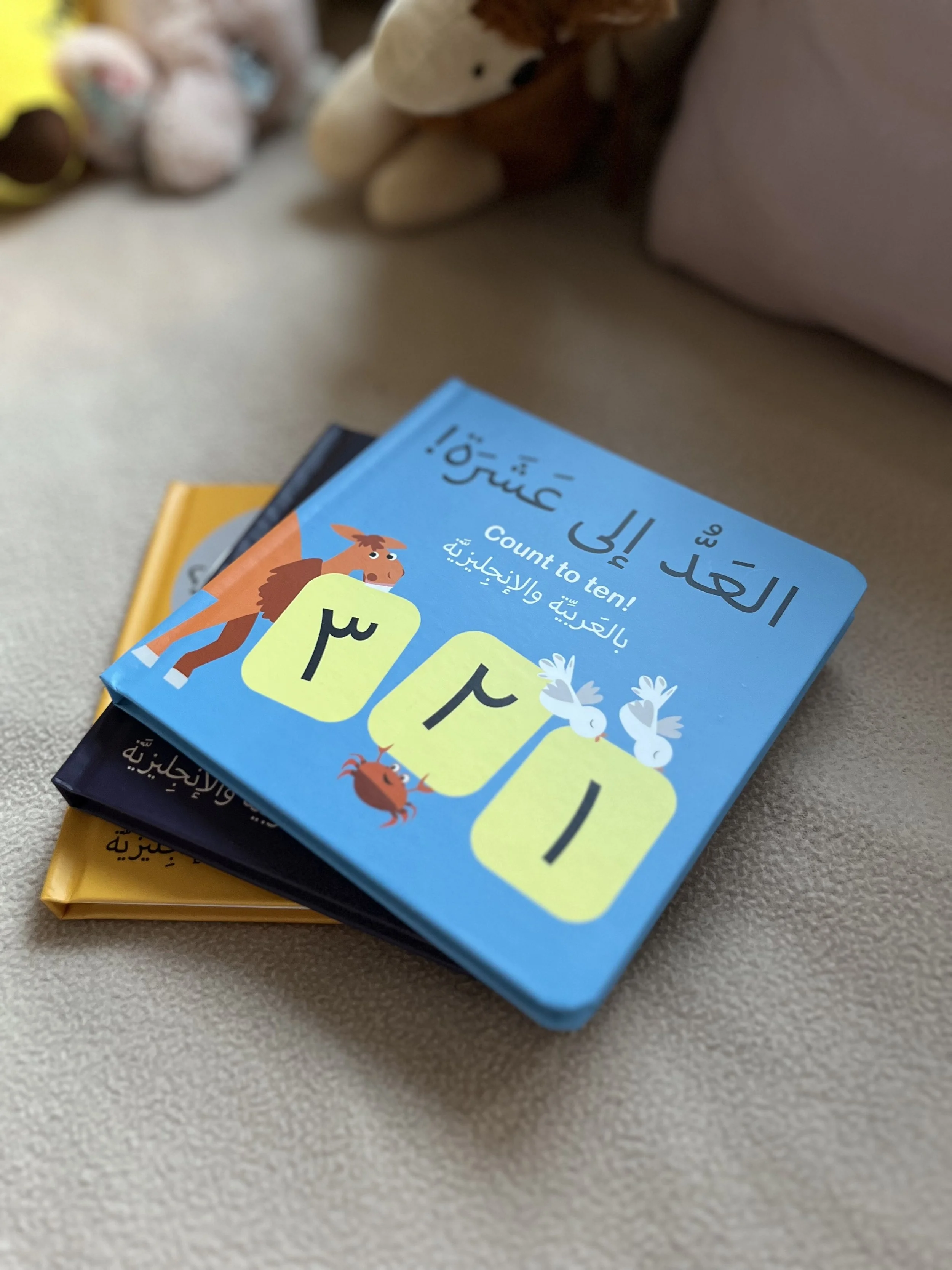 Count To Ten bilingual Arabic English children's book, placed on a soft surface with plush toys in the background.