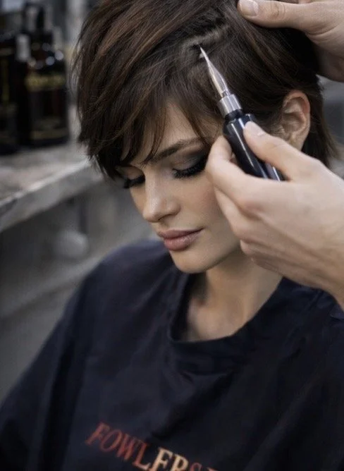 A woman receiving a cosmetic injection near her temple from a professional in a salon or clinic.