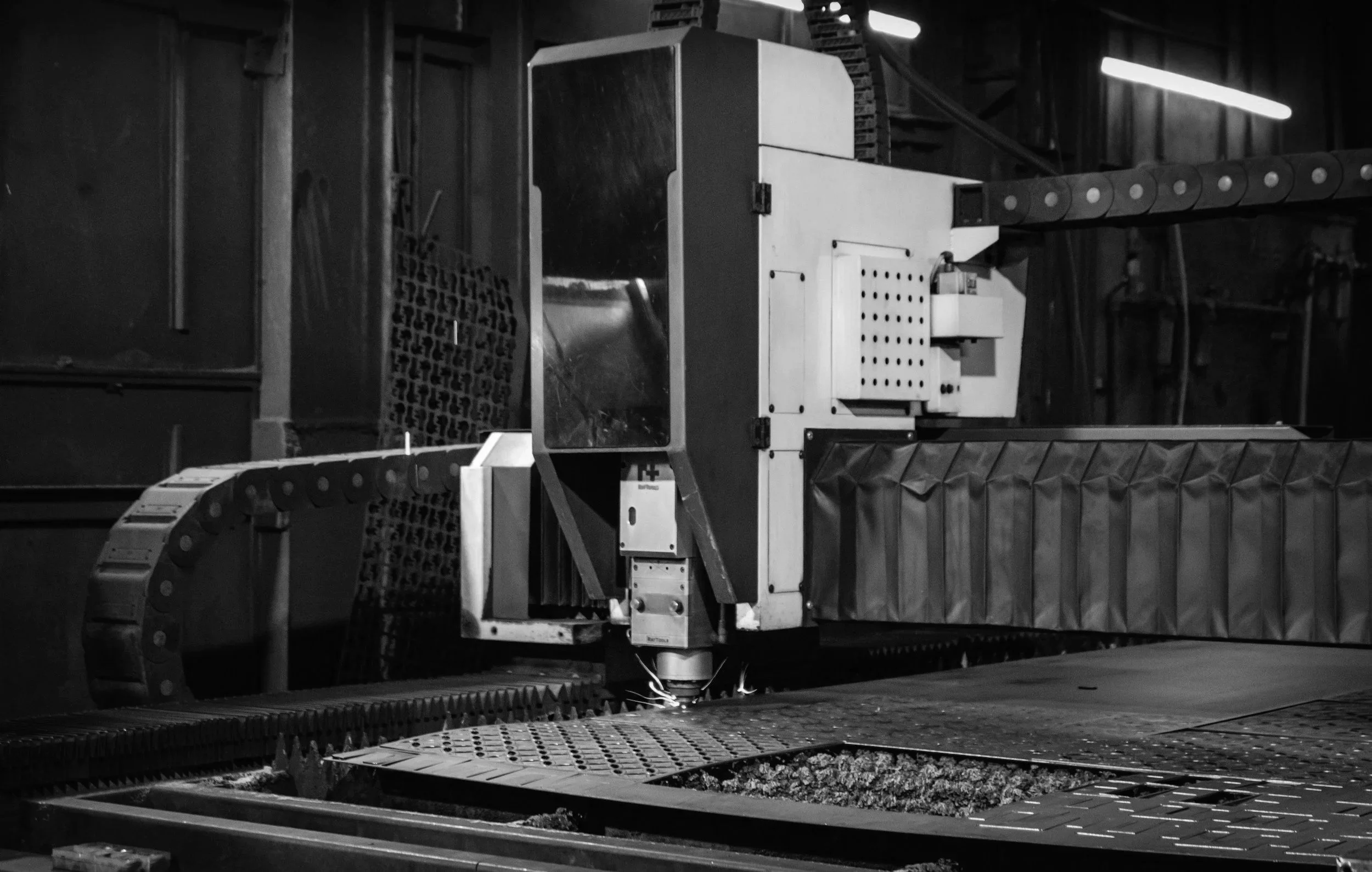 Black and white image of machinery in a workshop or factory, with metal parts and conveyor belts.