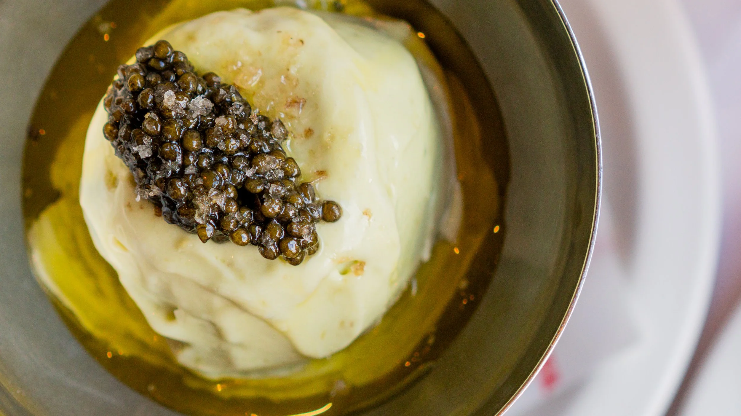 A scoop of vanilla ice cream topped with black caviar in a metal bowl.