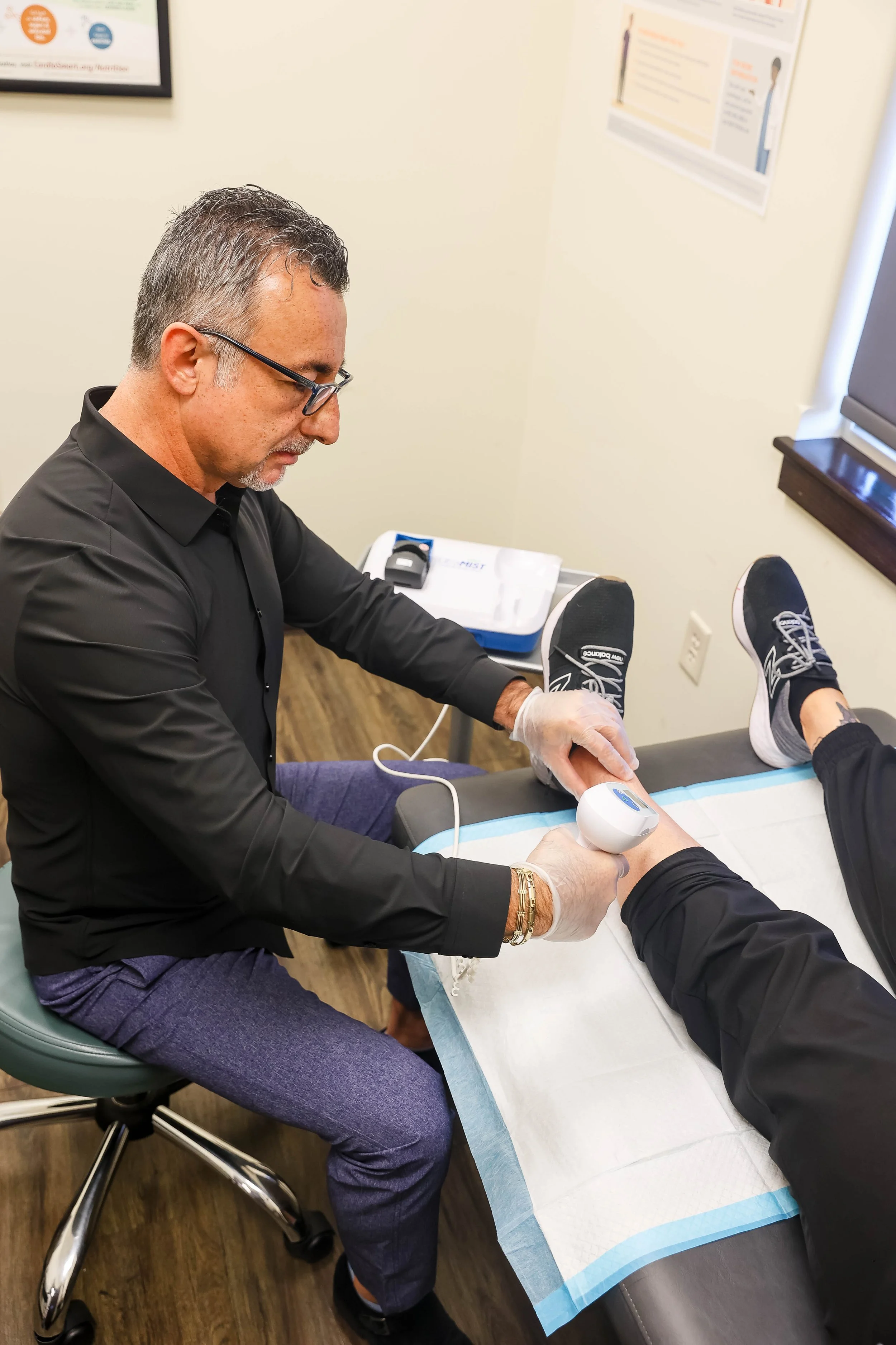 A healthcare professional using a handheld device to examine a patient's foot in a medical office.