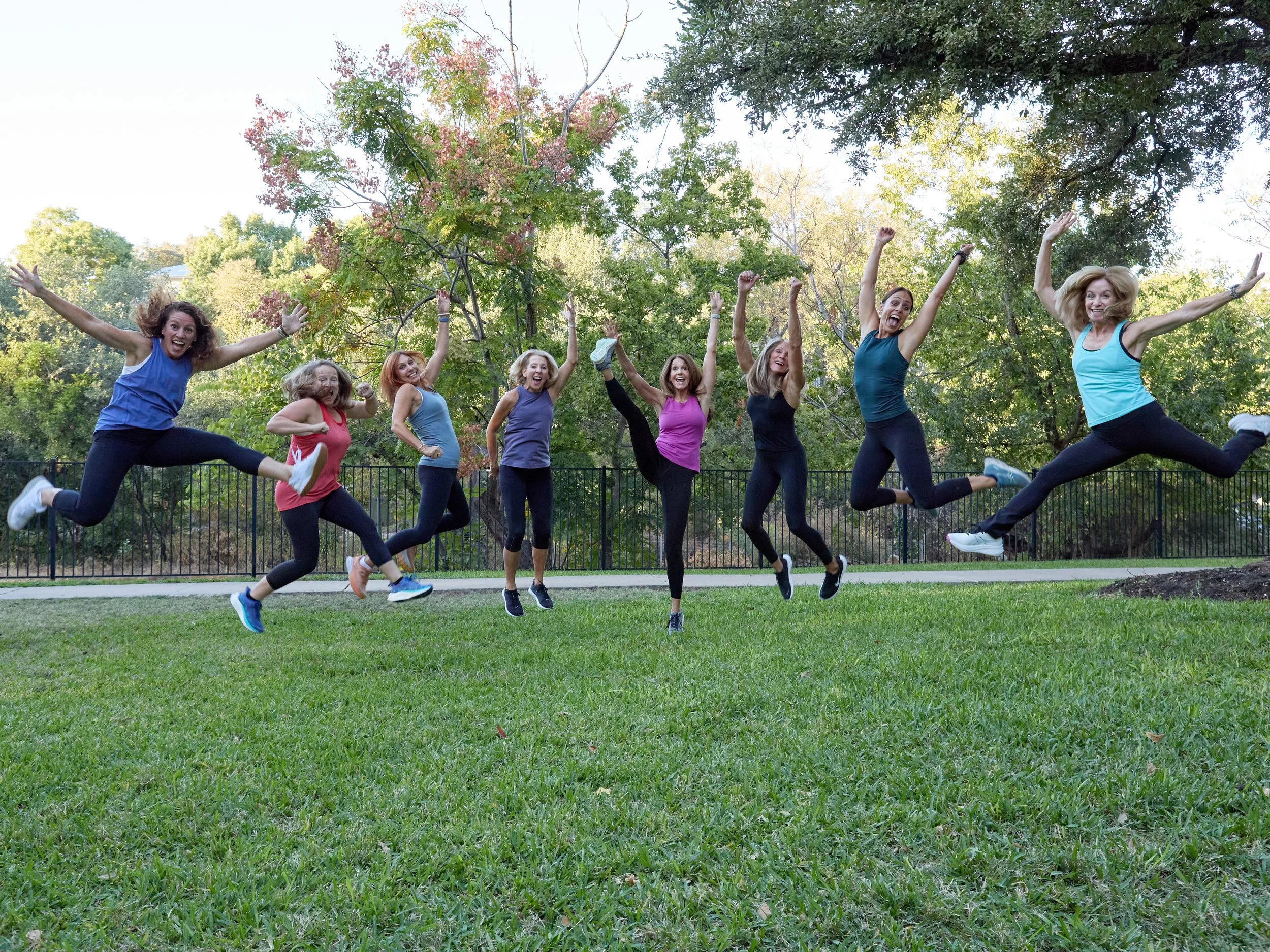 Women in colorful exercise clothes outdoors and jumping in green grass