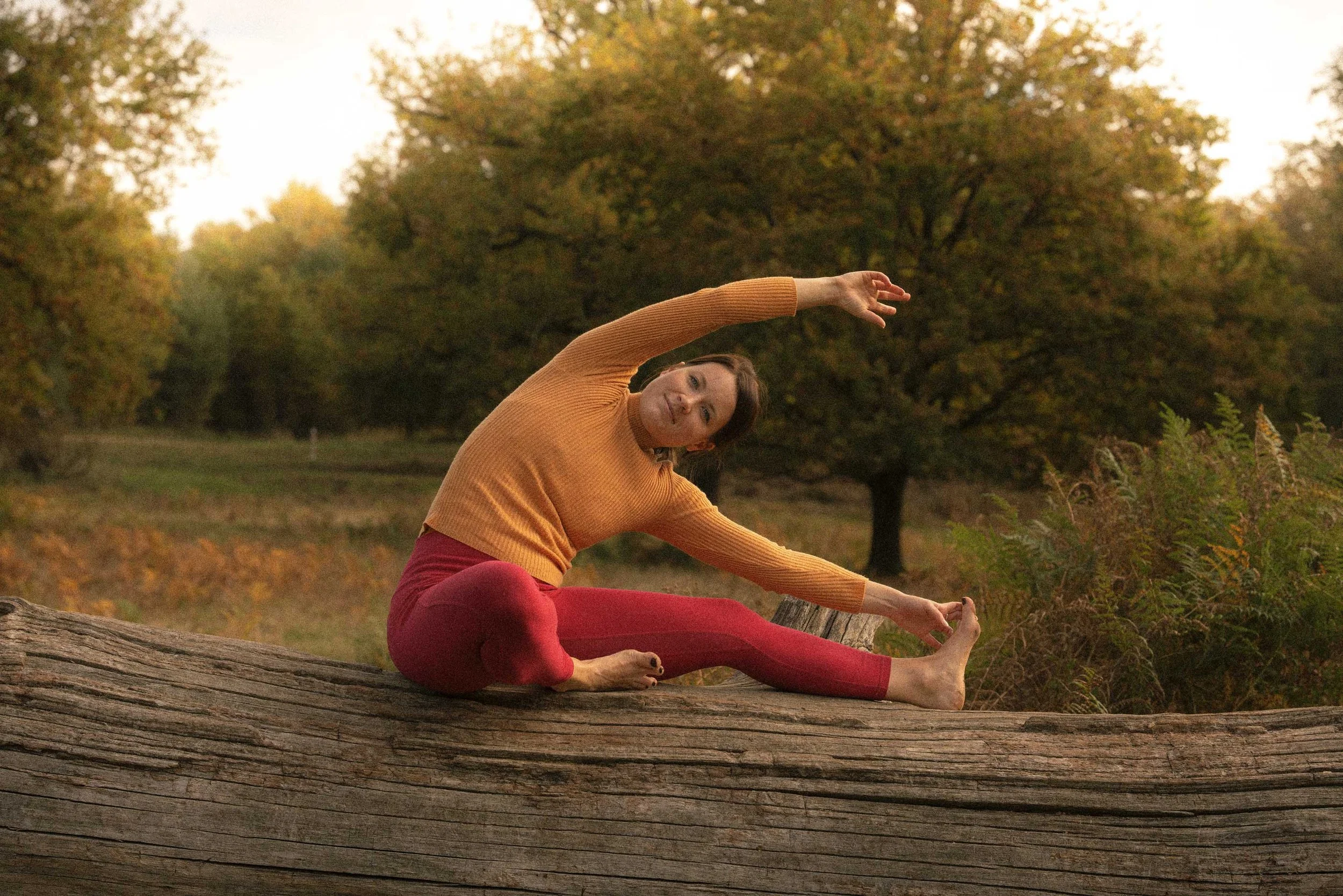Woman practicing yoga indoors, balancing on one hand with one leg raised and holding her foot with her hand, on a green yoga mat.