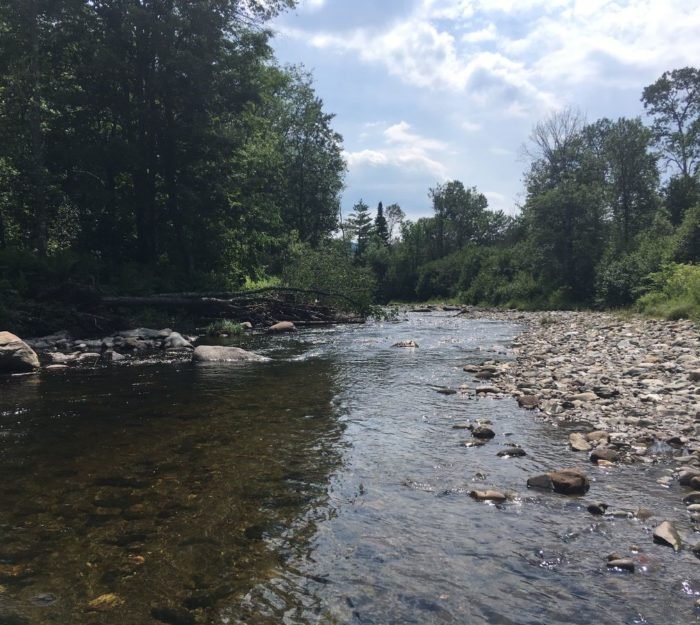 A calm, rocky river with trees on both sides under a partly cloudy sky.