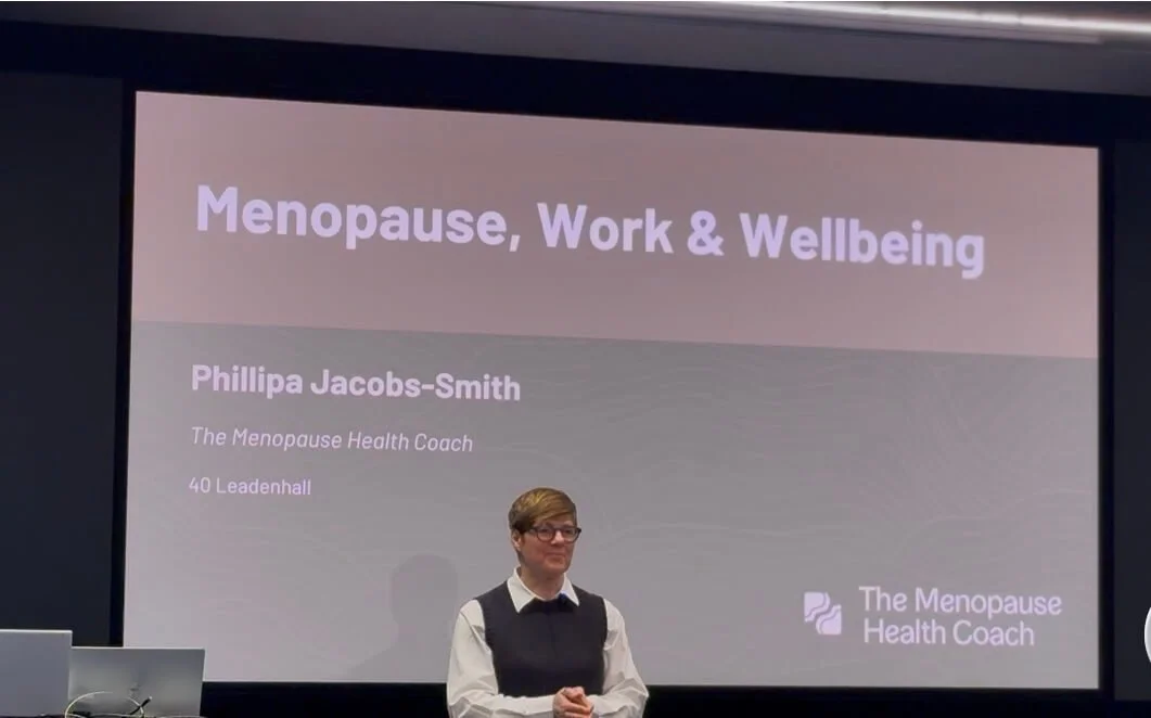Phillipa in a white shirt & blue sleevelss top an glasses standing in front of a presentation screen delivering a presentaion on Menopause, Work & Wellbeing at 40 Leadenhall, London, U.K.