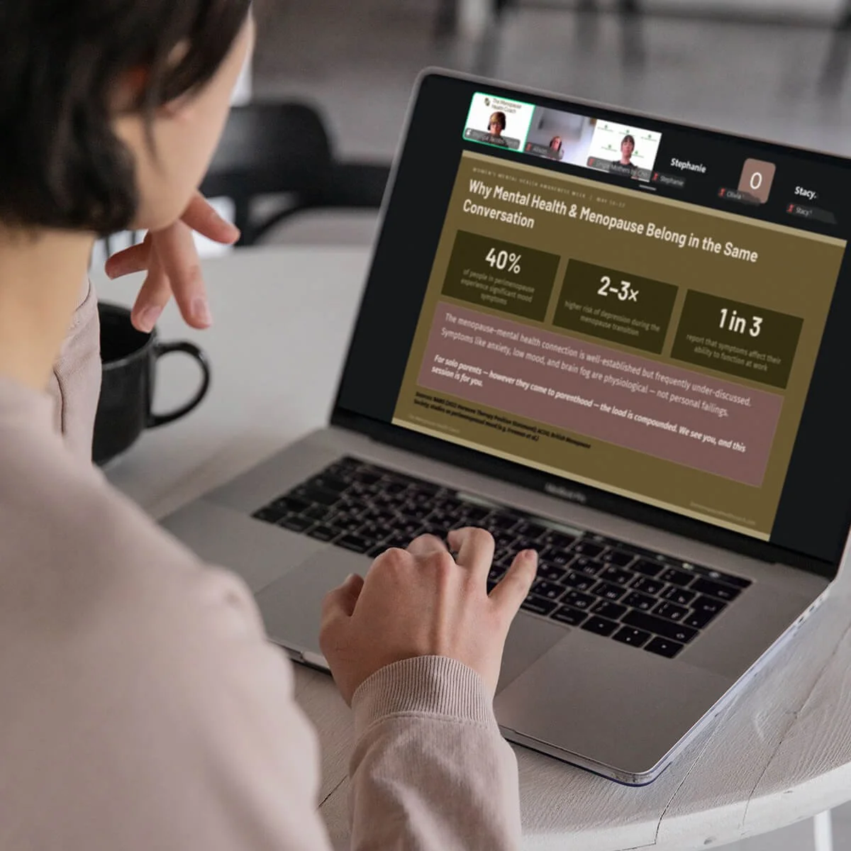 A person is sitting at a desk using a laptop to attend Phillipa's virtual presentation about mental health and menopause, with a focus on symptoms and statistics shown on the screen.