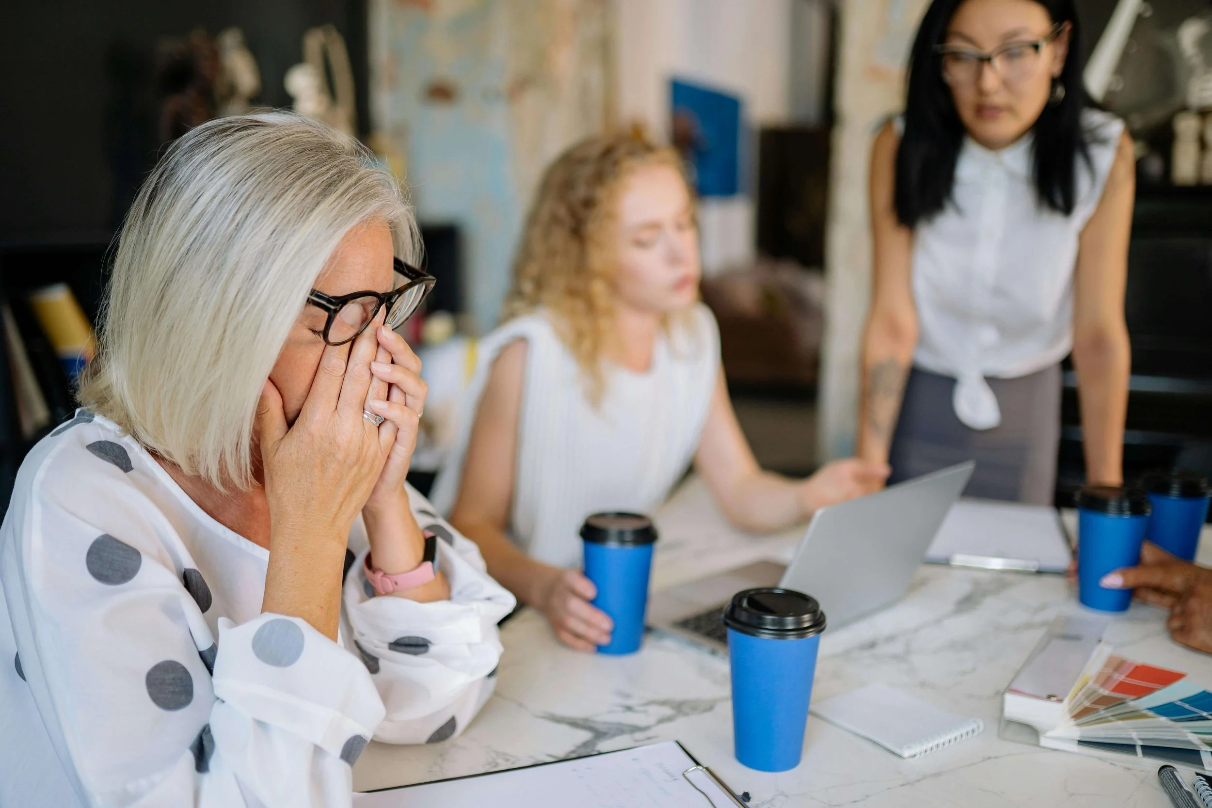 Office scene with women in a meeting, one with brain fog highlighting stress and teamwork dynamics