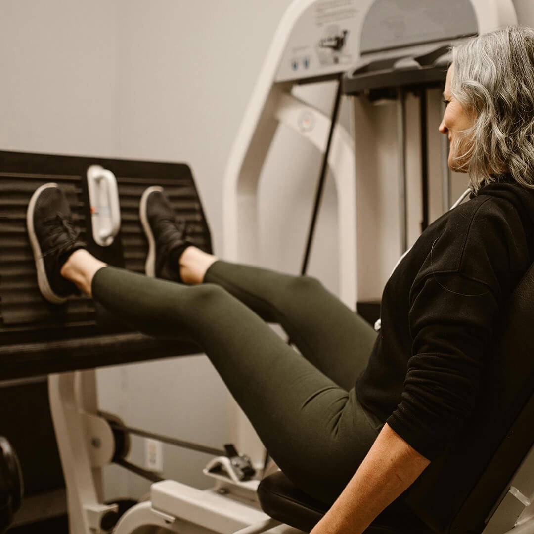 A woman exercising on a leg press machine at a gym.