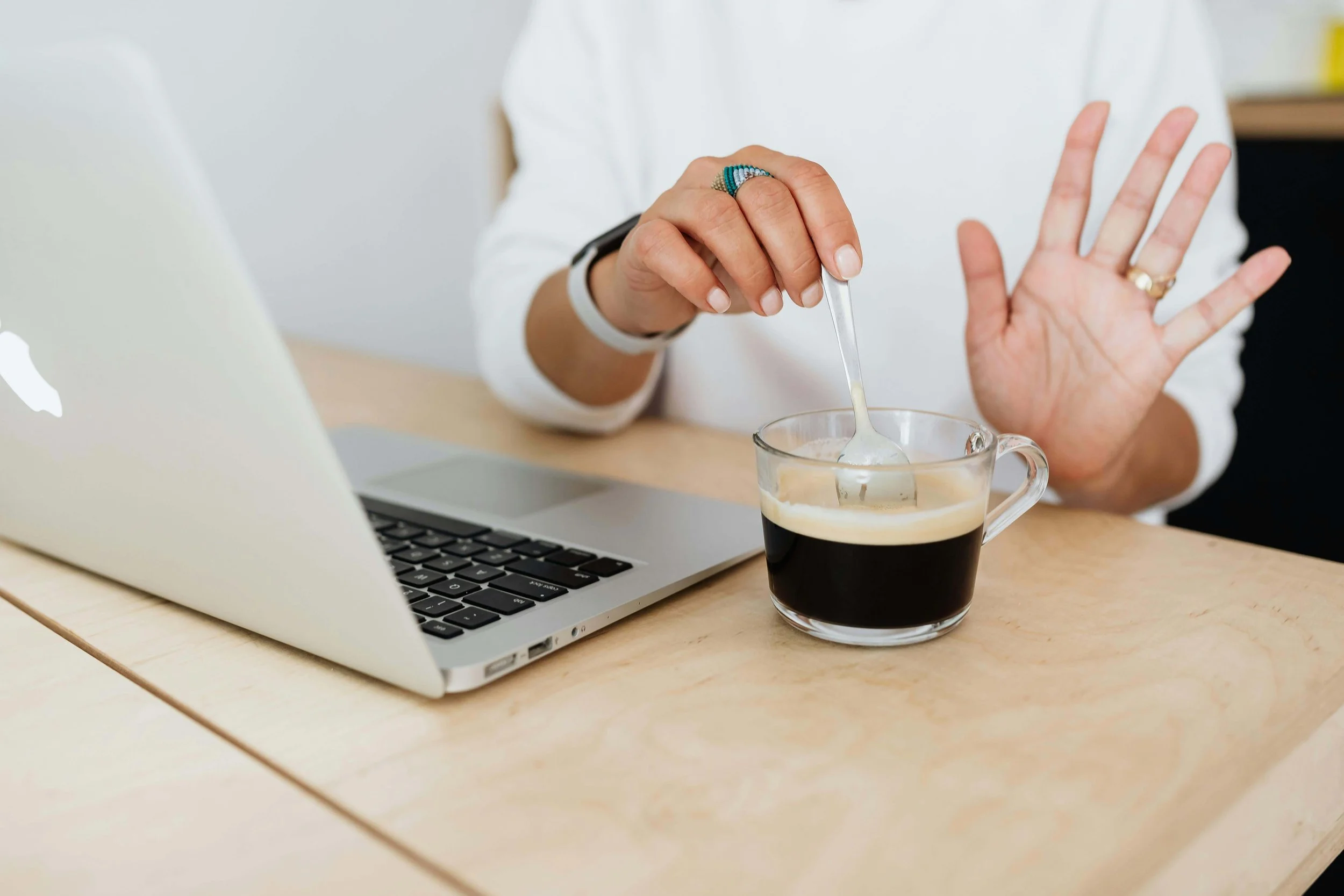 A woman stirs coffee beside a laptop at a desk, highlighting work fatigue & managing energy lows