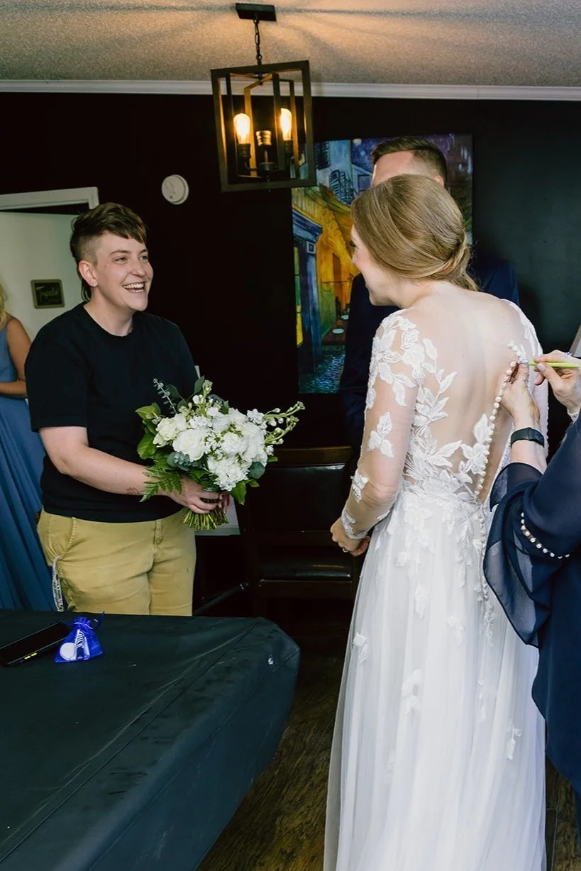 florsit Karit giving the Bride her bouquet as bride get her buttons on her dress together