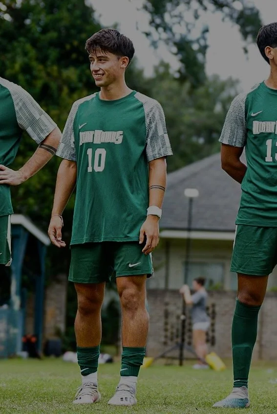 Grupo de jóvenes en uniforme de fútbol en un campo, con árboles y una casa en el fondo.
