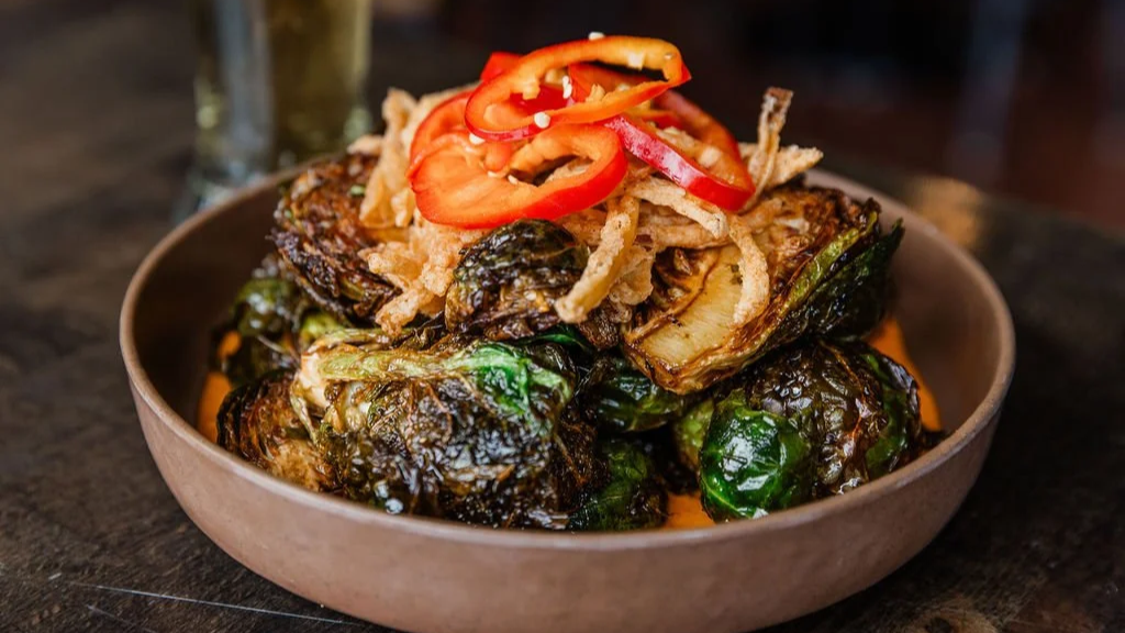 A bowl of roasted Brussels sprouts topped with shredded fried onions and slices of red bell pepper.