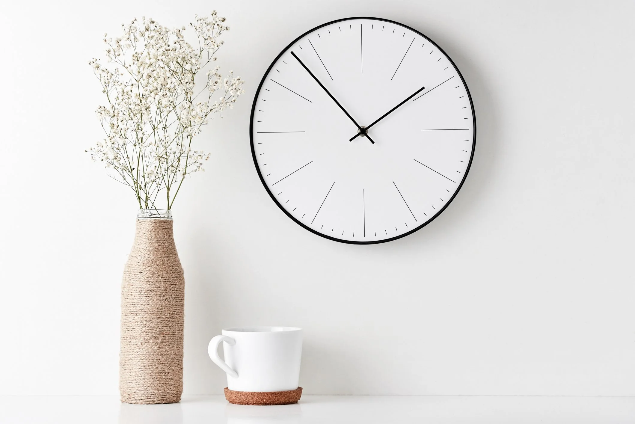 Minimalist wall clock with vase of dried flowers and white coffee cup on table.