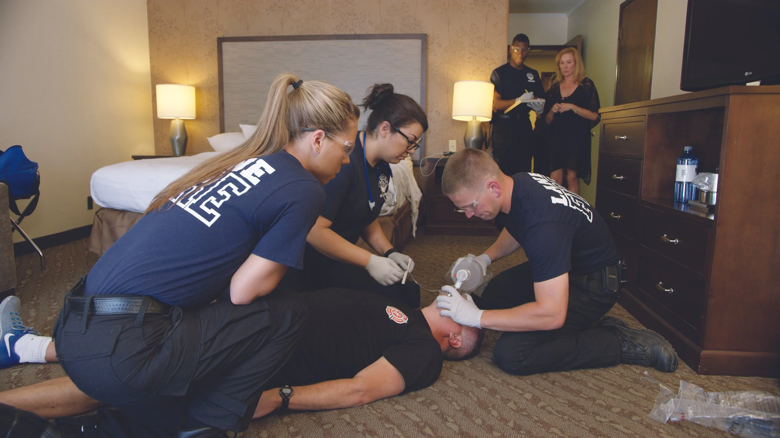 Emergency responders providing medical assistance to a person lying on the floor in a hotel room.