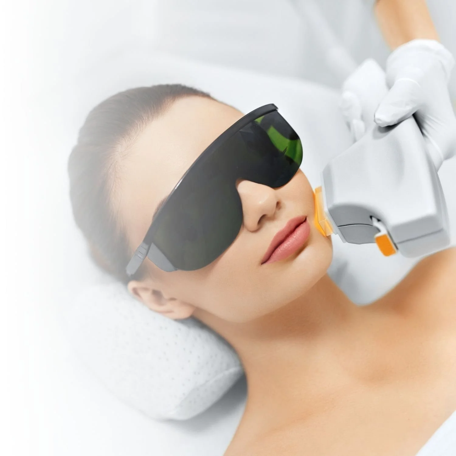 A woman receiving a facial laser treatment, wearing protective eyewear, with a gloved hand holding the laser device.