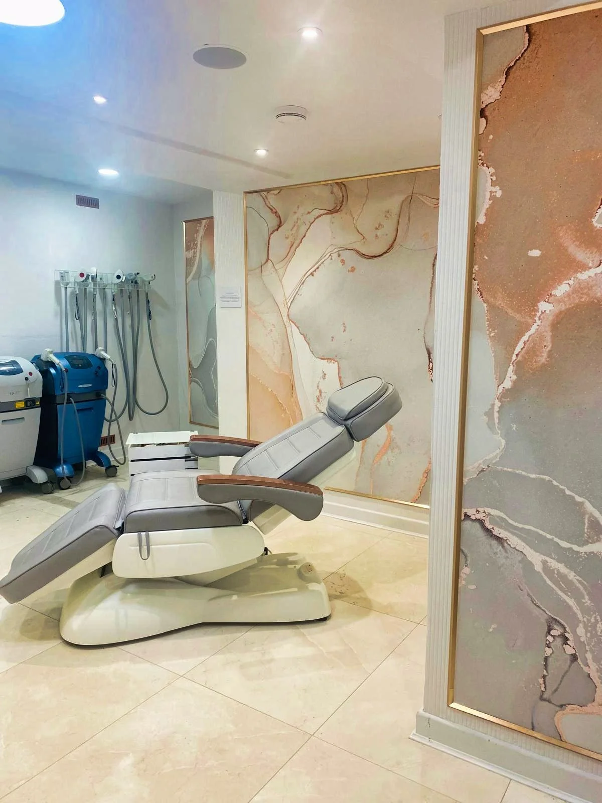 Medical treatment room with adjustable reclining chair, marble-patterned walls, and medical equipment in the background.