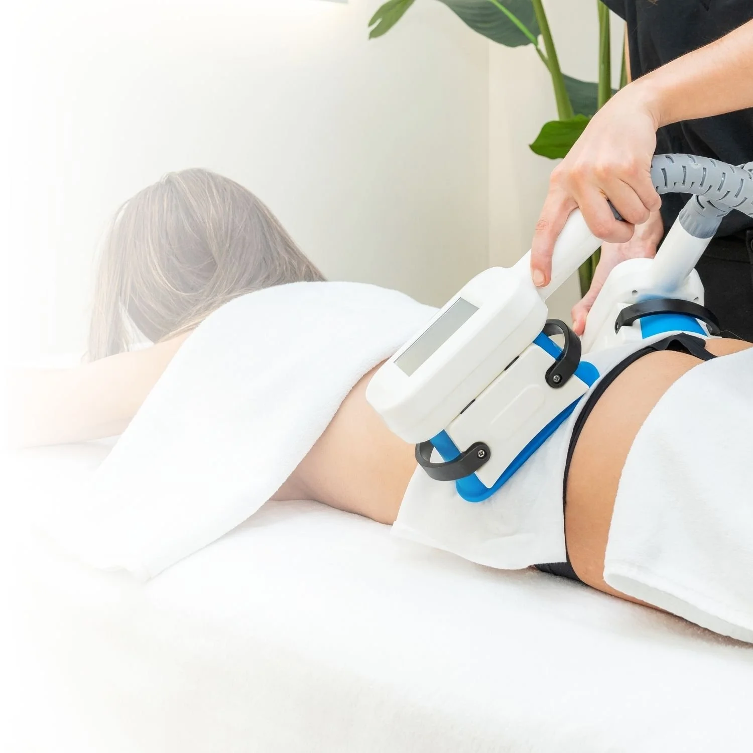 A person receives a treatment with a medical device on their lower back while lying face down on a white treatment table.