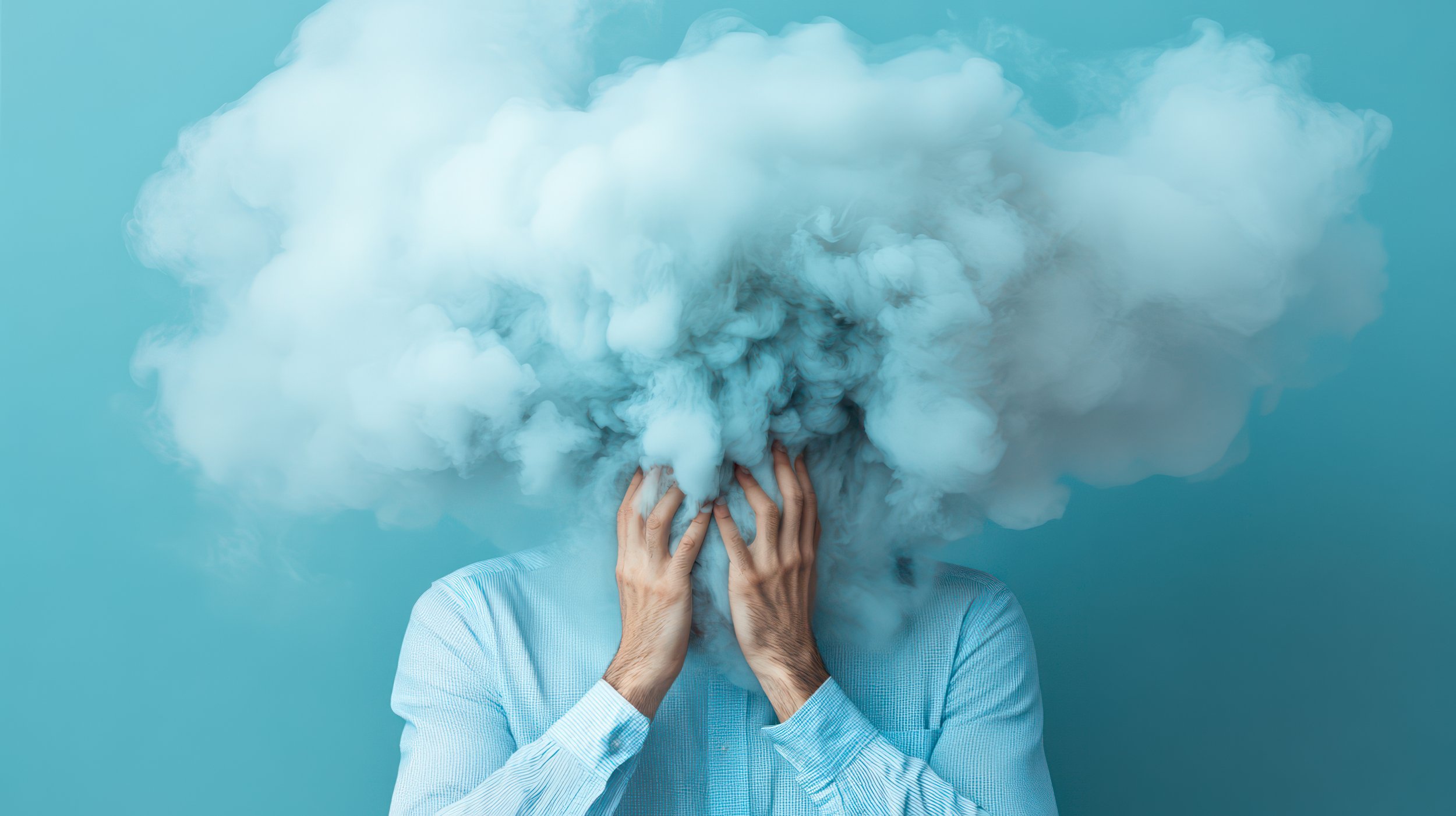A person in a light blue shirt covering their face with hands, with a large cloud of blue smoke obscuring their head, against a matching blue background.