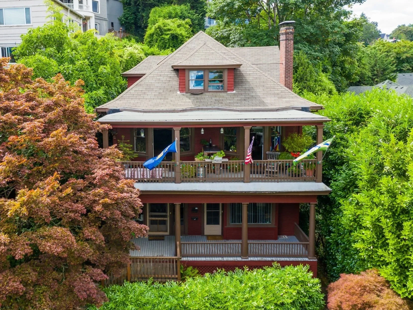 A multifamily family house in SW Portland near Portland State University. A three-story red house with a porch and balcony, surrounded by green trees and foliage.