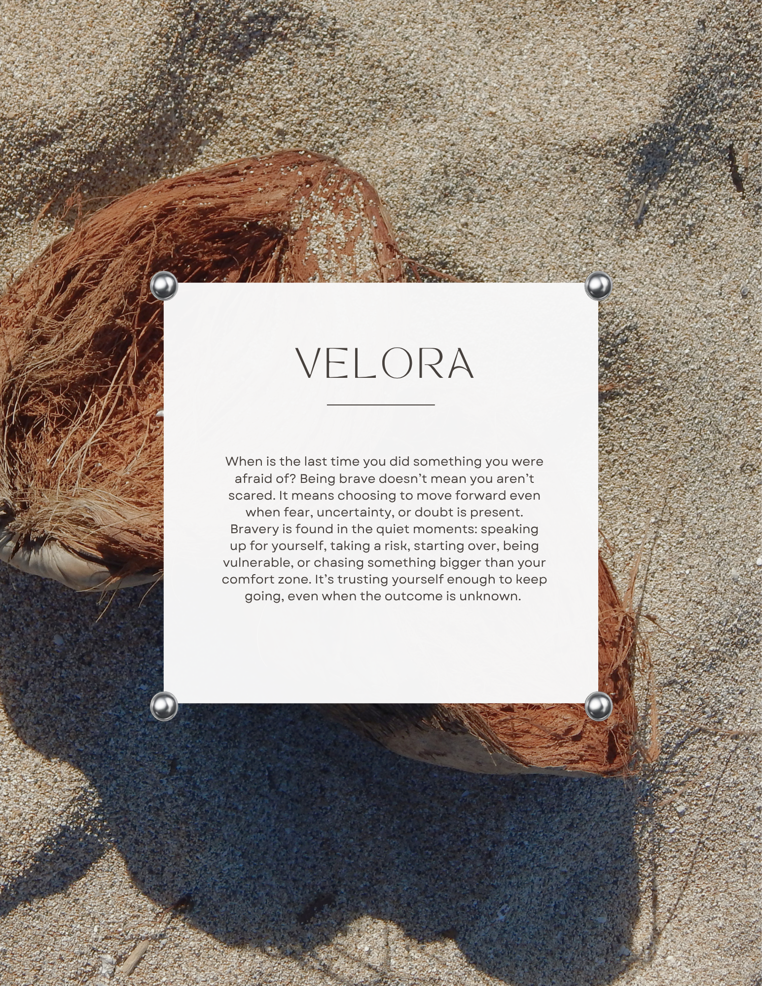 Close-up of a coconut shell with a paper note on it that reads 'Velora' and an inspirational quote, on sandy ground.