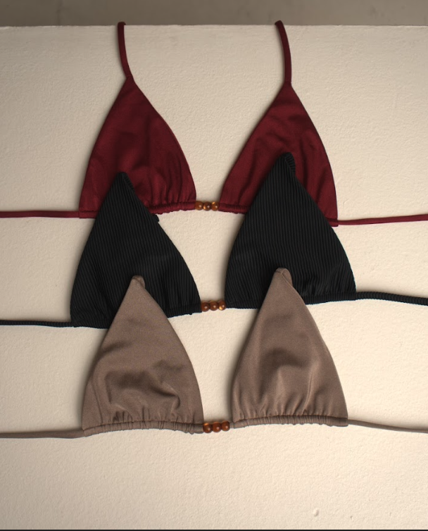 Three bikini tops in red, black, and beige hanging on a white wall.
