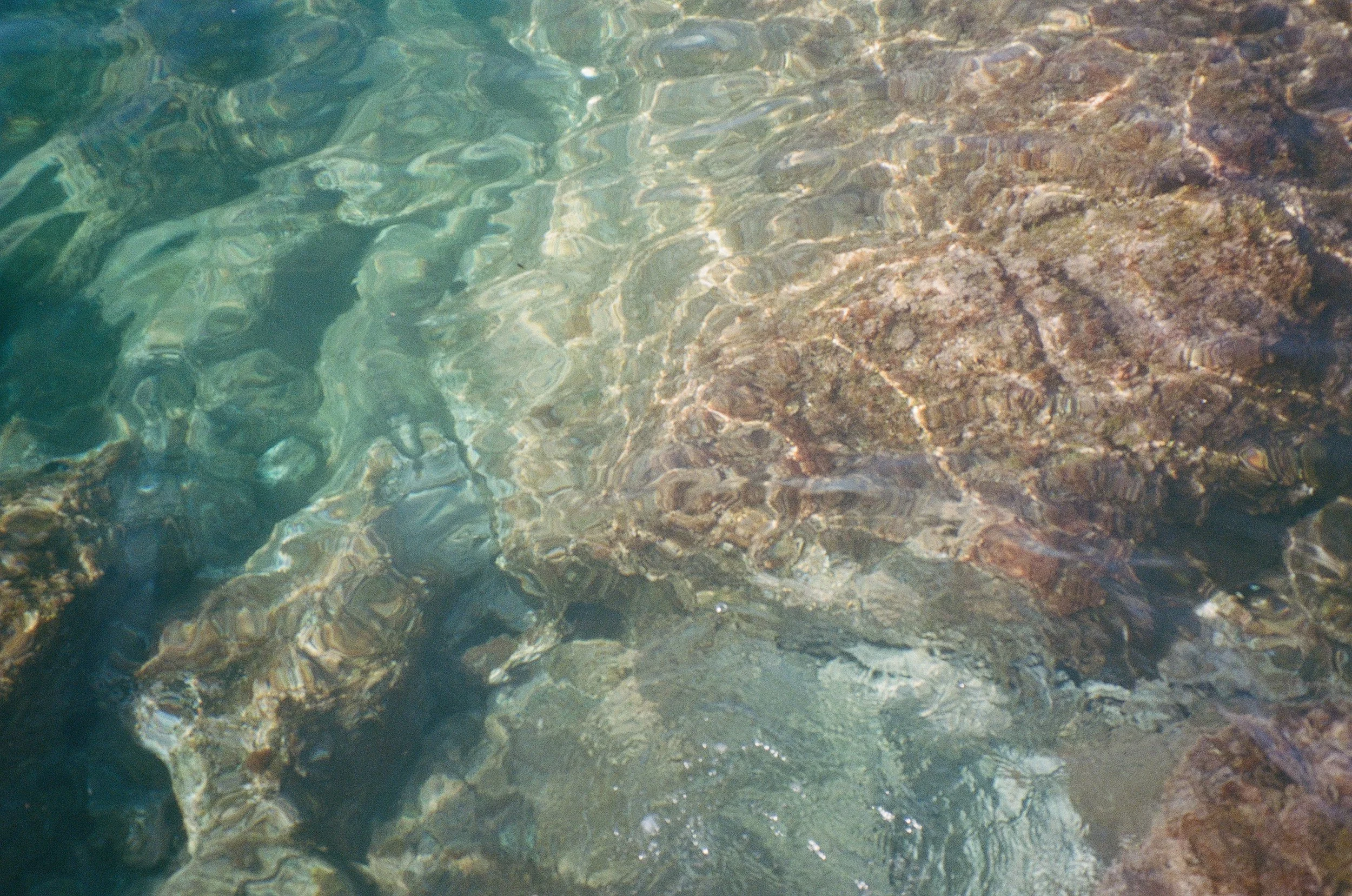 Clear water over rocks and sand at the bottom of a shallow stream or river.