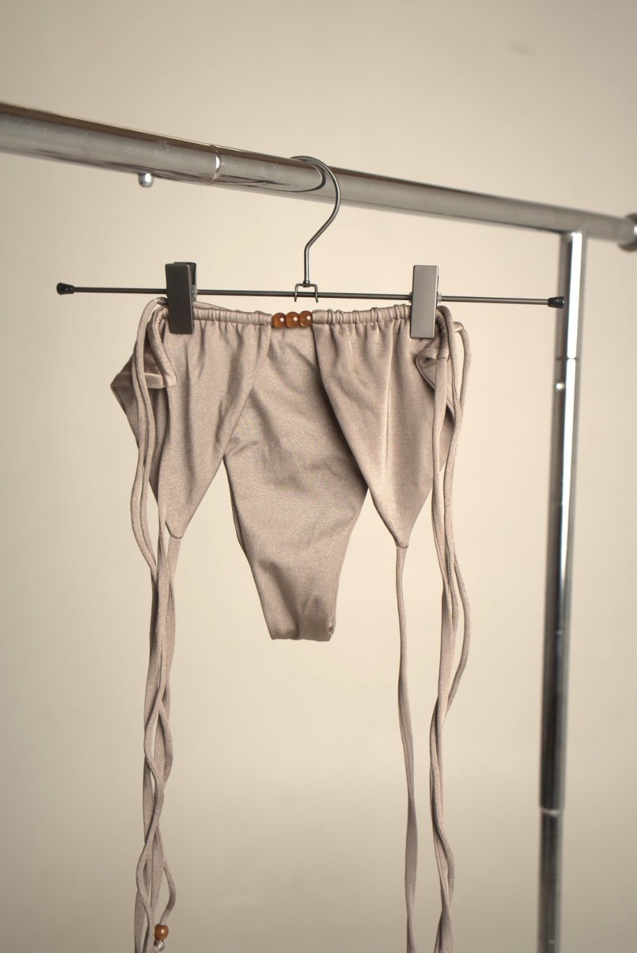 A pair of beige underwear with long strings hanging on a metal clothing rack.