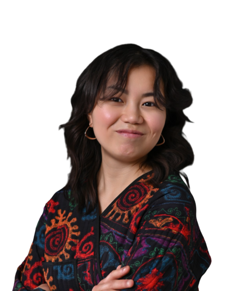 A woman with dark, wavy hair and hoop earrings smiling with crossed arms, wearing a colorful, patterned jacket against a plain white background.