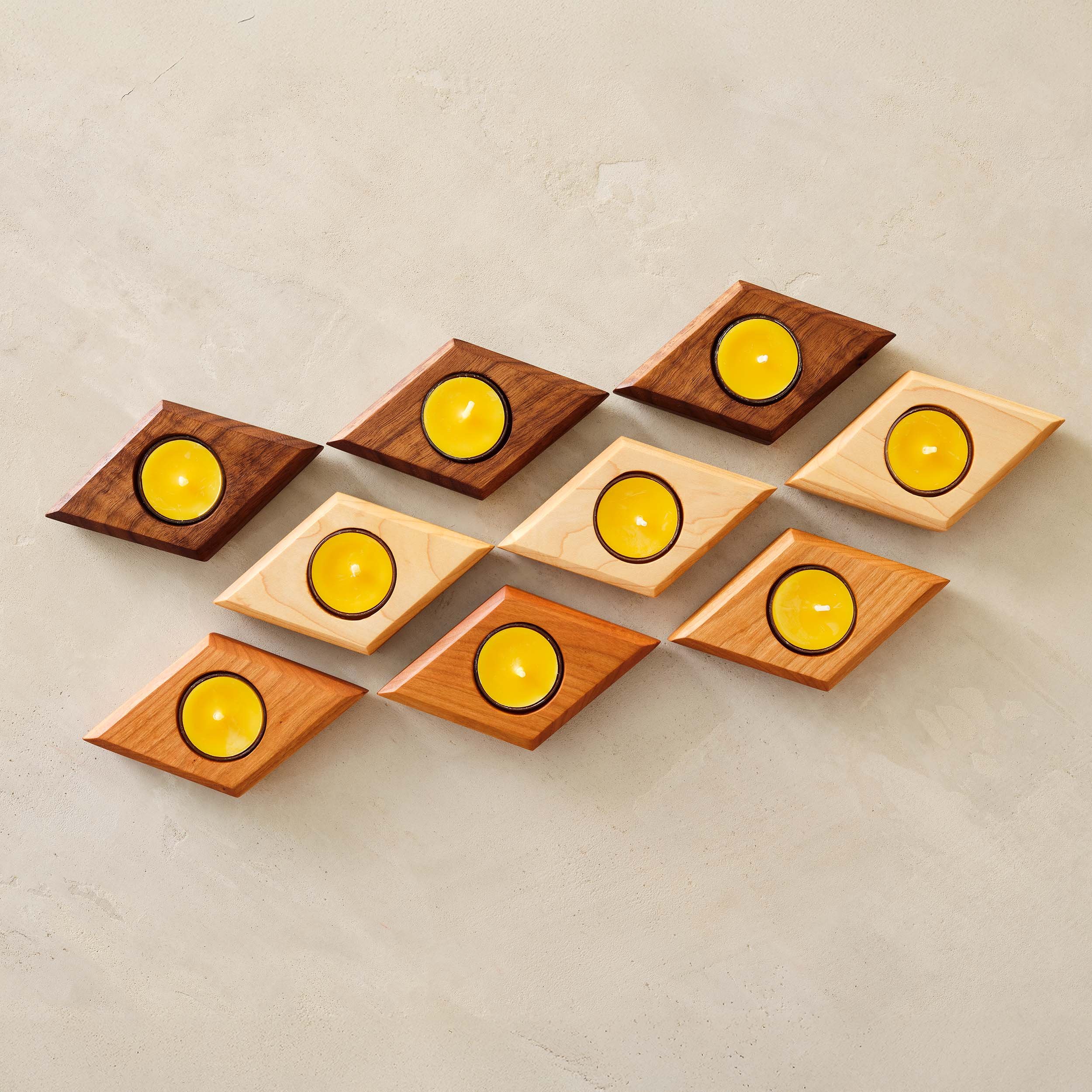 9 diamond shaped tealight holders with candles, 3 in brown walnut, 3 in yellow maple, and 3 in red cherry