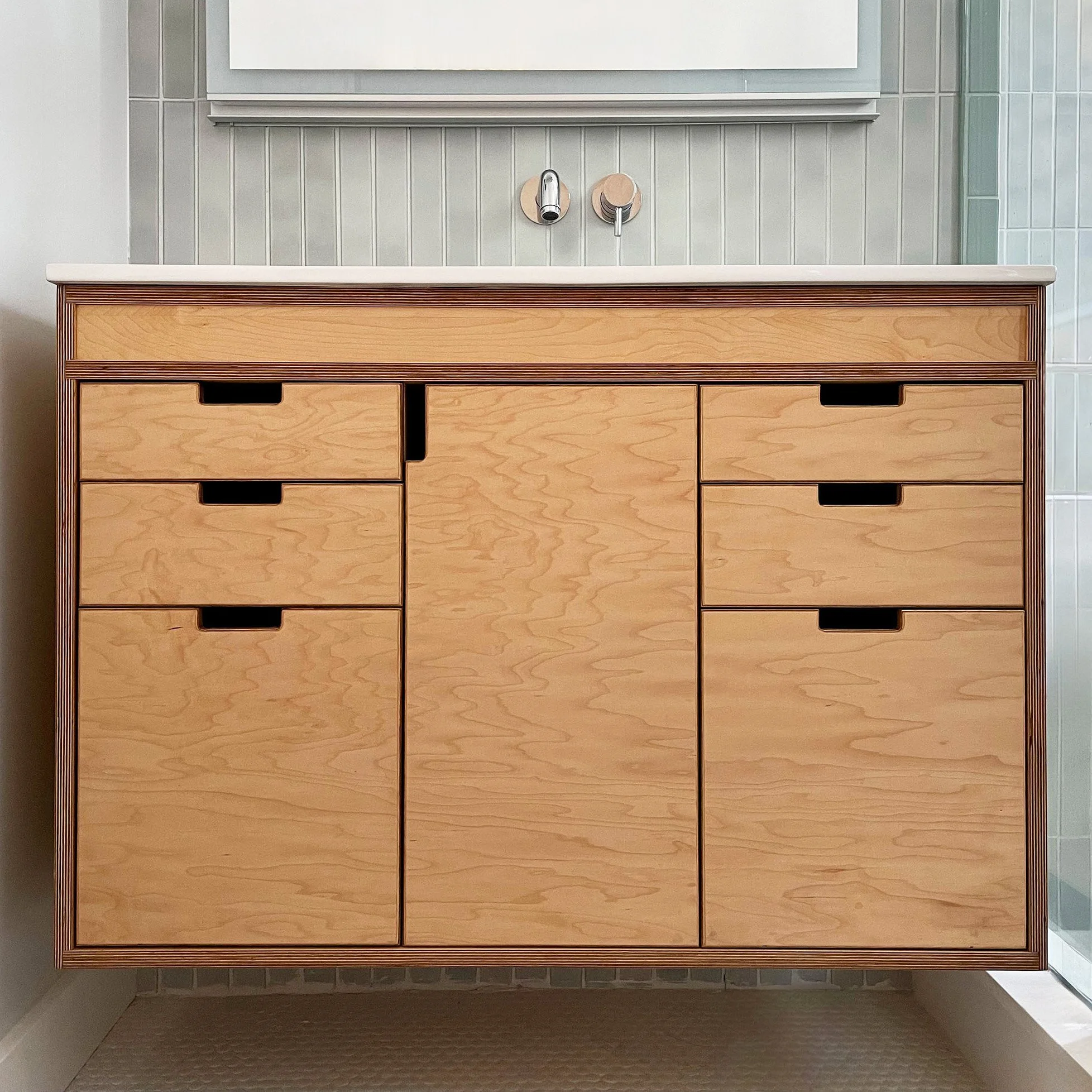 Wooden bathroom vanity with nine drawers and cabinet doors, white countertop, and wall-mounted faucet and fixtures.