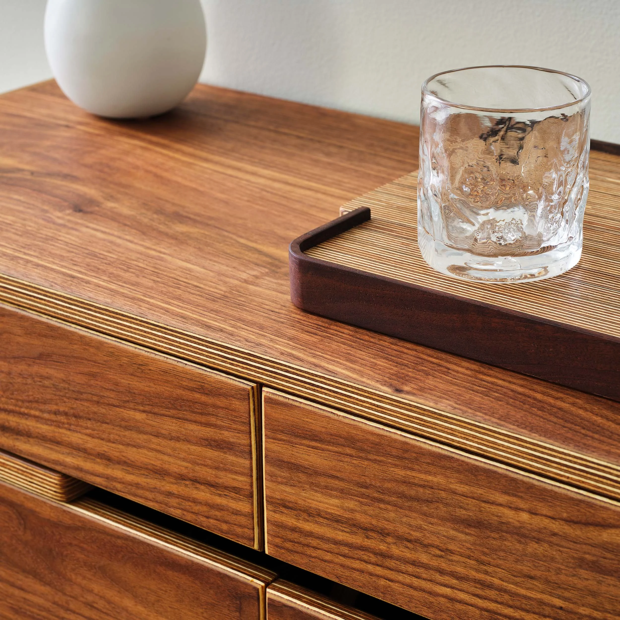 Close-up of a wooden cabinet with a clear glass and a wooden tray on top.