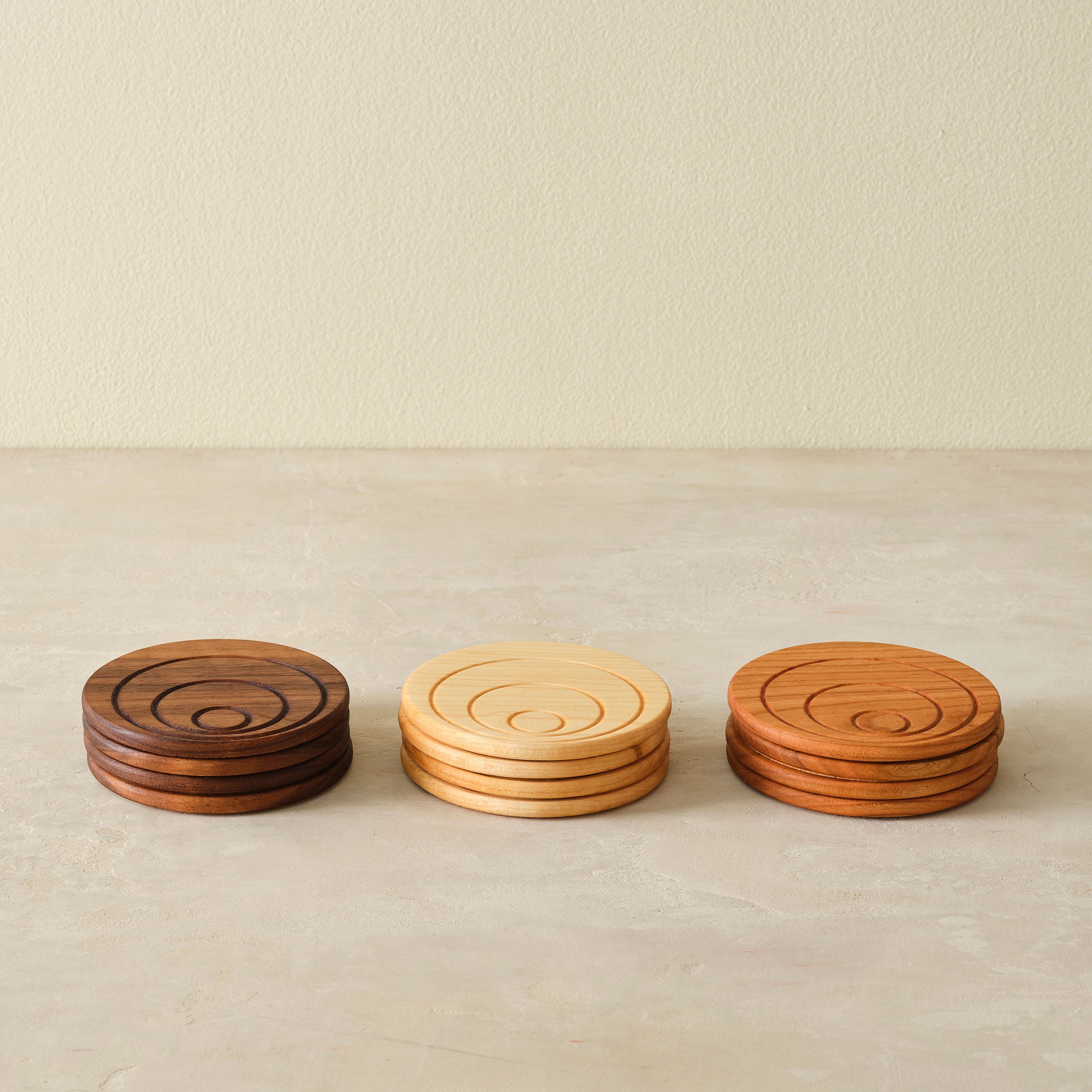 four stacks of wooden coasters with circles carved into them. Left stack is dark brown, middle stack is yellowish, right stack is reddish orange.