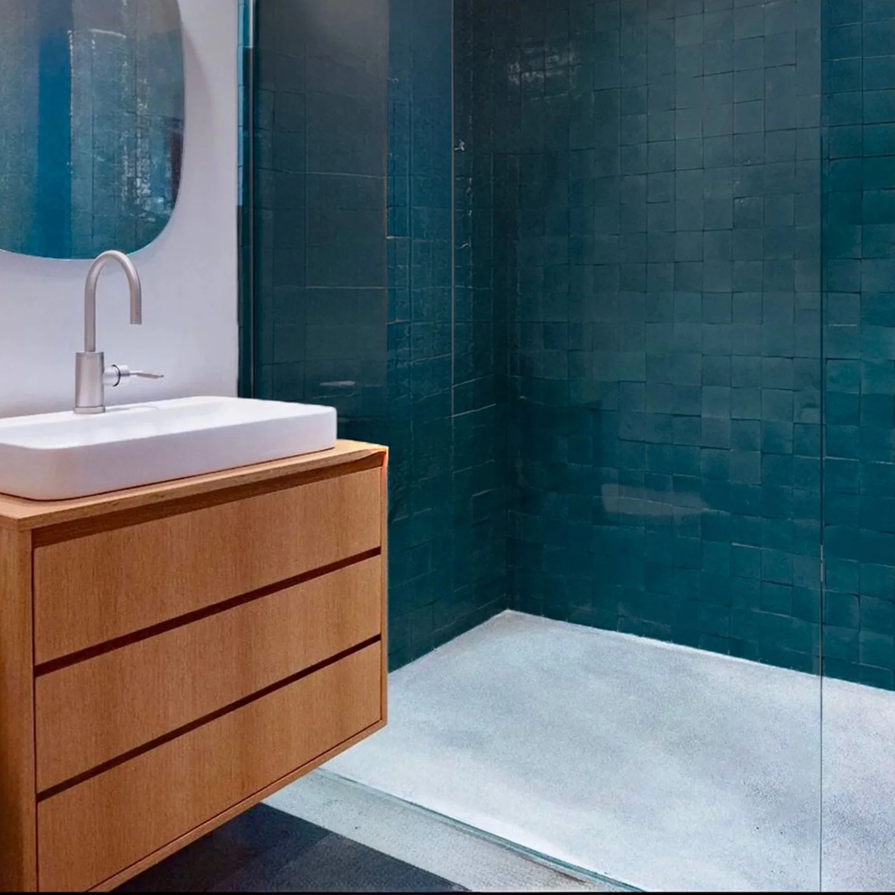 Modern bathroom with a wooden vanity, white vessel sink, silver faucet, large mirror, and a walk-in shower with blue tiled walls and white floor.