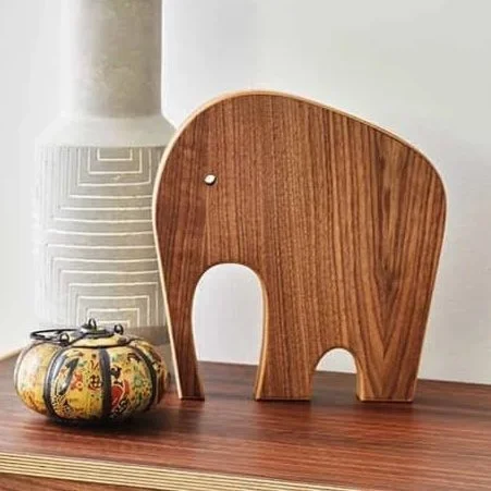 Decorative wooden elephant sculpture on a table, with a tall white vase and a small colorful decorative object nearby.