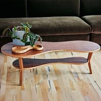A two-tone wooden coffee table with a potted plant on top, positioned in front of a dark gray sofa on a light wood floor.