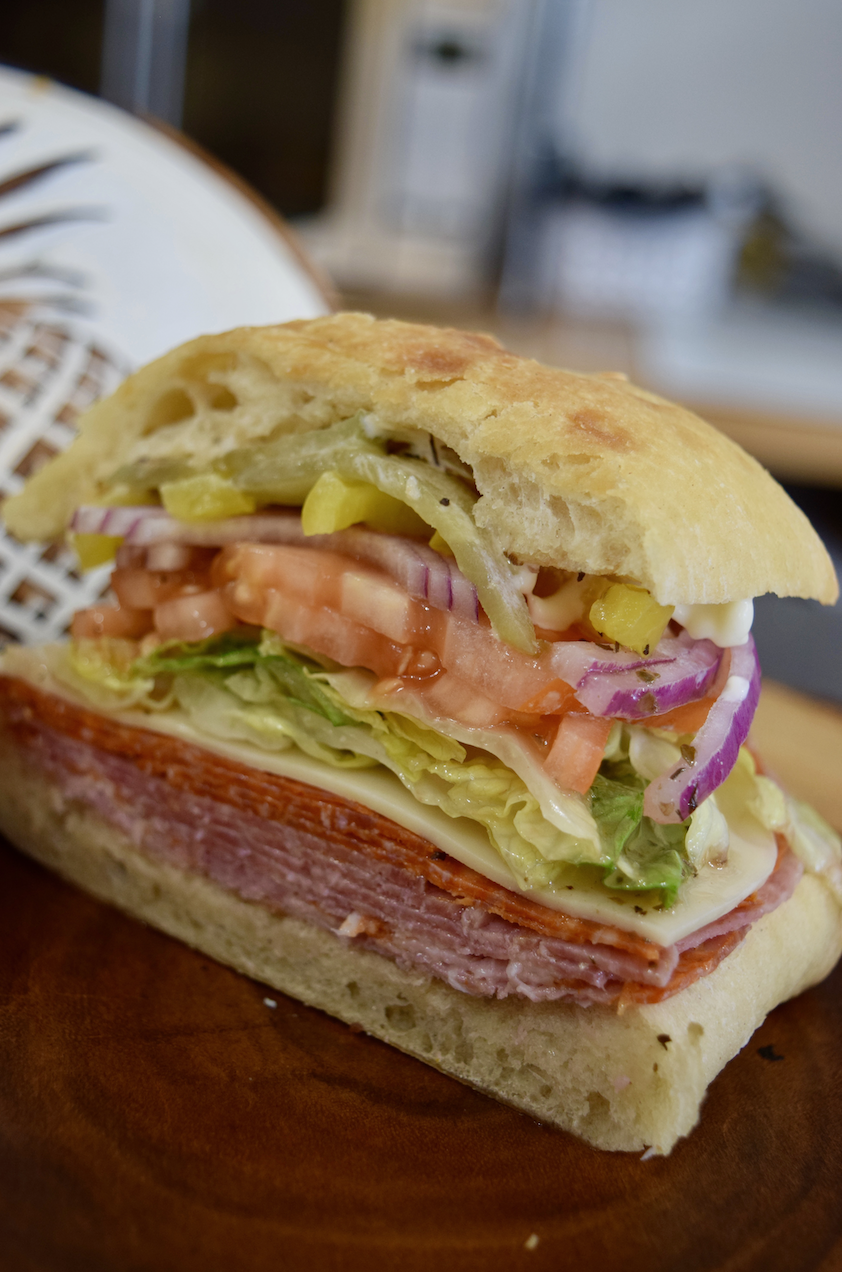 Italian sandwich with salami, ham, cheese, lettuce, tomato, onion, and peppers on ciabatta bread