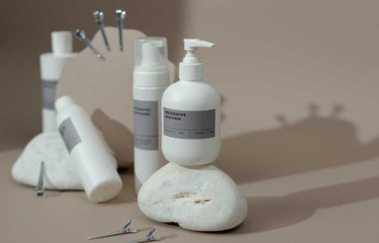 Hair care products, including a restorative hair mask and moisturizing conditioner, displayed on rocks with metal clips; neutral background.