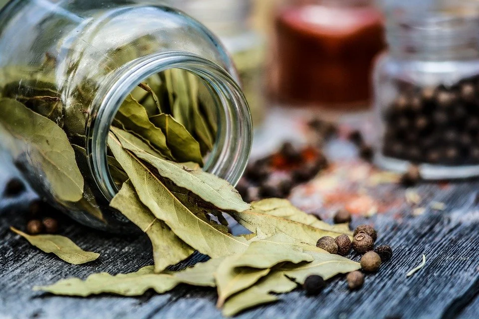 Glass jar with dried bay leaves spilled on table, peppercorns